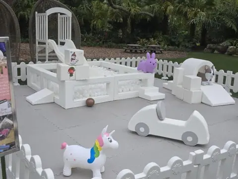 White soft-play pen with slide and ride-on toys on the lawn