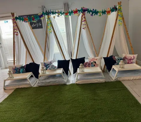 Row of white sleepover teepees with navy pillows and breakfast trays