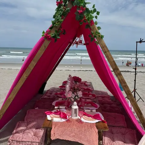 Hot-pink beach teepee with a low table set on the sand