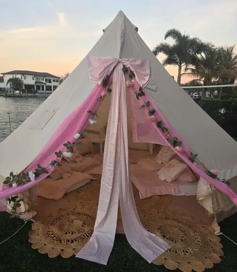 Bell tent with a pink bow and blush drapes on a waterfront lawn at sunset