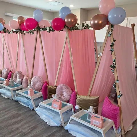 Row of pink sleepover teepees with trays, pillows and a balloon garland